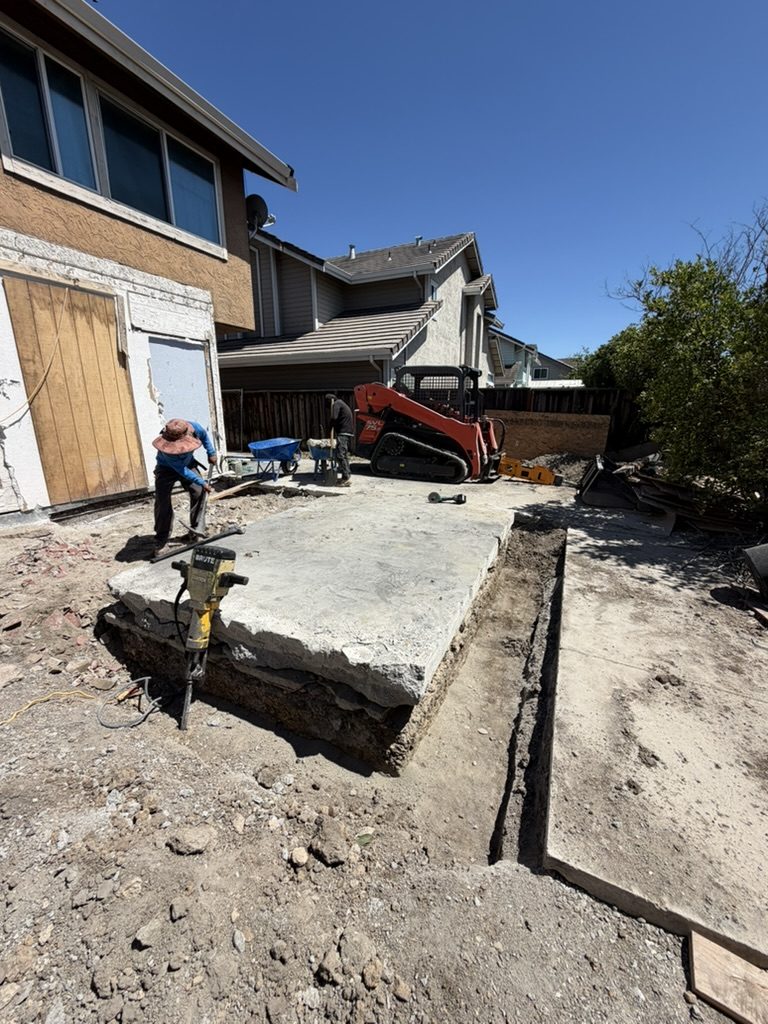 Crew cutting into the existing concrete slab at a Milpitas home addition, with a section lifted showing it was not a structural slab