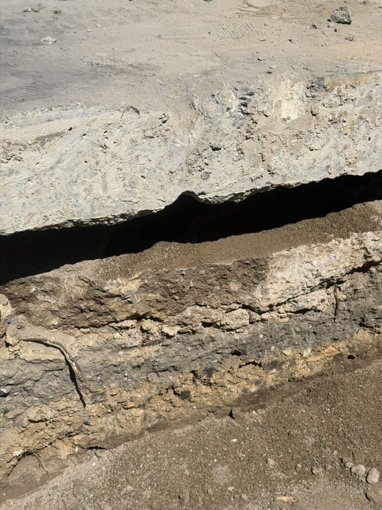 Close-up of the sand and fill layer separating two concrete slabs, with corroded wire visible